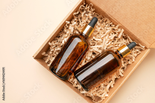Glass cosmetic bottles with dropper brown amber color in packaging craft cardboard box on beige background. Natural cosmetics mockup, serum or face oil flat lay top view. Concept of beauty, branding