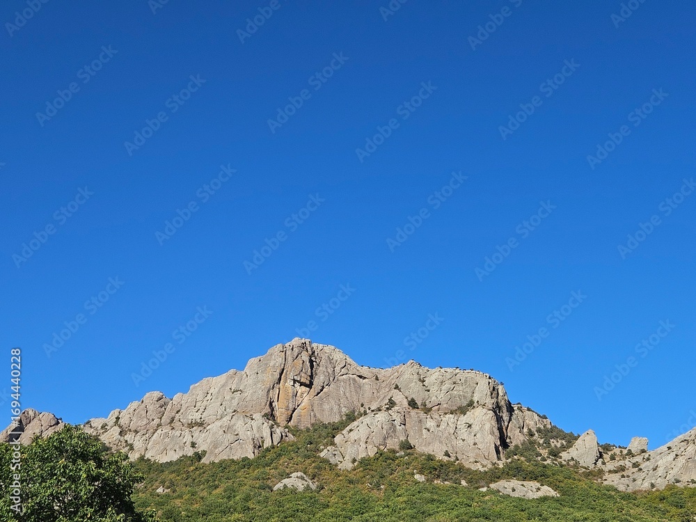 Fototapeta premium Majestic rocky mountain against a vast, clear blue sky. Perfect for travel themes, motivational content, or as a website banner with ample copy space for text.