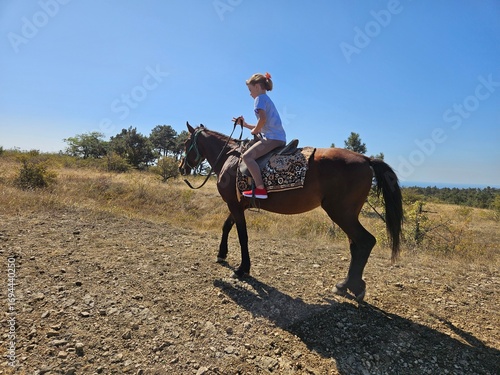 A young girl enjoys a horseback ride on a scenic mountain trail on a sunny day. Ideal for content about travel, family vacations, outdoor adventures, and active hobbies.