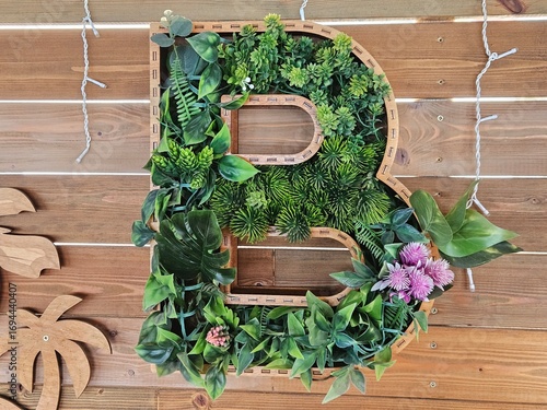 Creative wooden letter 'B' filled with faux succulents and green plants. Rustic eco-decor for events, interiors, or personalized branding on a wooden background.