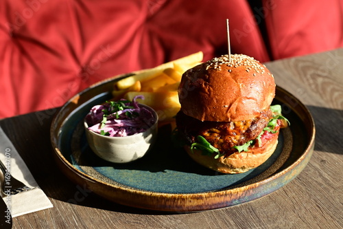Juicy burger served with golden French fries on a plate in a restaurant setting. A classic and appetizing meal, perfect representation of comfort food and casual dining.