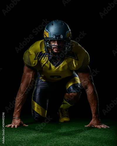 Strong American football athlete in yellow gear kneeling on grass, symbol of determination and power. Great for sports media, motivational design and championship themes.