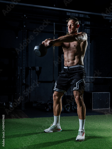 Muscular man training with weights. Brutal strong athletic men pumping up muscles workout in dark gym.