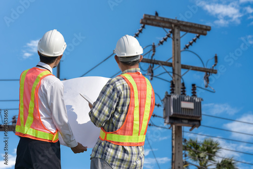 Electrical engineer with two workers talking to each other working and checking work at a transformer poles. Engineers look at the work and plan the high voltage poles.