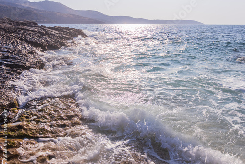 Sunlit turquoise shallows ripple gently against a rugged rocky coastline. The scene blends luminous water clarity with the timeless texture of coastal stone, evoking peace, warmth, and natural beauty.