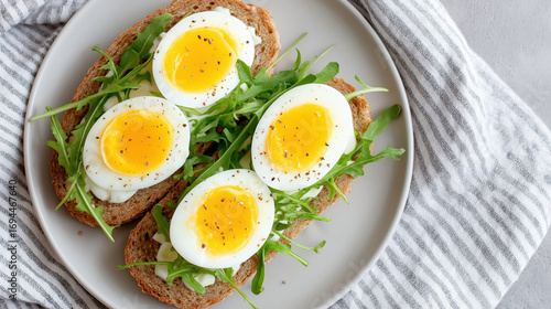 Soft boiled egg slices on whole grain bread with fresh arugula and black pepper served on white plate for healthy meal