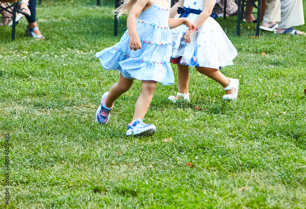 Two girls in fancy dresses run on grass at open-air city festival. Concept: city festivals, summer, holidays
