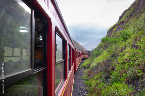 View from a classic red train as it curves through lush, green mountain slopes. This dynamic shot captures the immersive experience of a scenic railway journey through breathtaking natural landscapes.