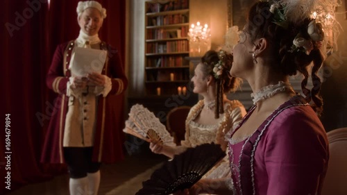 Medium shot of young 19th century Caucasian gentleman serenading two mature ladies with own song and reciting poems, while excited noblewomen are listening, waving fans and admiring talent