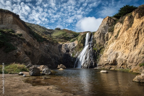 Waterfall cascading into a secluded pool, surrounded by rugged cliffs and hills