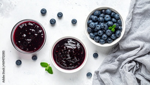 Blueberries and blueberry jam arranged in white bowls with mint leaves on a light surface, evoking freshness, richness, and artisanal food styling.