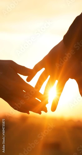 Close-up of the silhouettes of a couple in love holding their hands together, romantic scene at sunset, slow motion. The man and woman have their hands clasped tightly and the golden sun