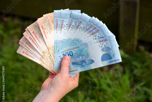 Close-up of adult hand holding bunch of Brazilian Reais notes of value 100 and value 50 with defocus background. Photo taken September 9th, 2025, Zurich, Switzerland.