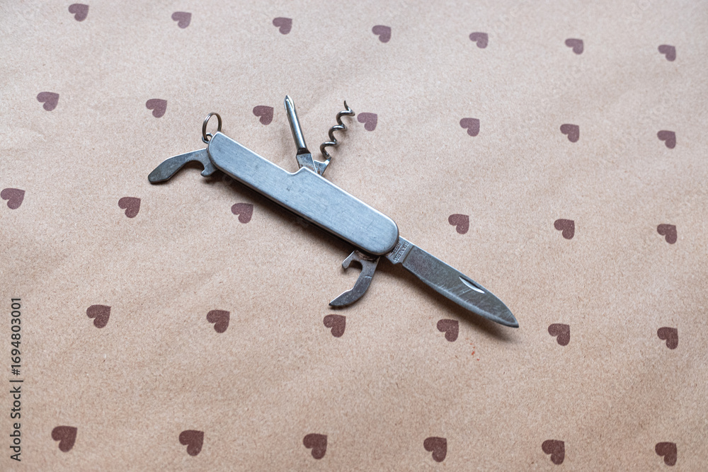 Obraz premium A classic metal multi-tool pocket knife on a heart pattern background, Versatile Tool