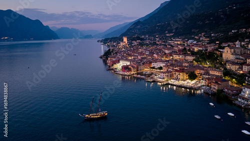 Malcesine at Sunset - Aerial View: Breathtaking drone shot of Malcesine's historic town and Scaliger Castle. The beautiful Italian village glows with night lights as the sun sets over Garda Lake.