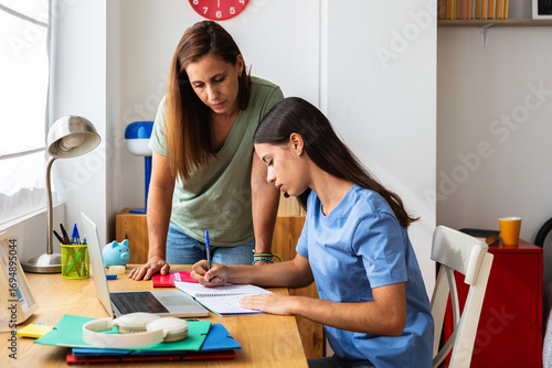 Wallpaper Mural Mid adult mother helping teenage daughter with her homework while studying on laptop in her bedroom. Back to school and education lifestyle concept Torontodigital.ca