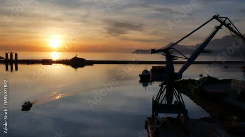 Beautiful sunset in the port of Bar, Montenegro. Calm water with reflections, pilot boat and tug moving across the port basin, and mountains in the background.