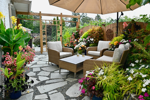 Outdoor seasonal backyard luxurious flagstone patio with cozy seating and tropical gardens and flowering planters
