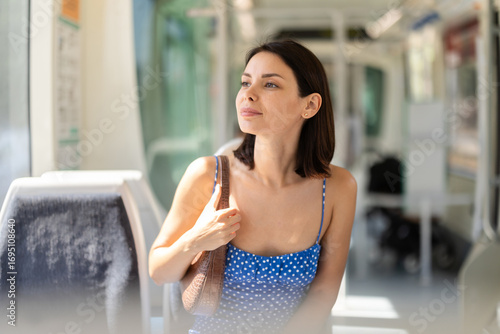 Elegant young female passenger sitting and looking around in bright modern train