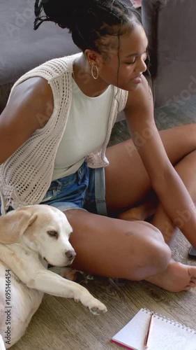 Vertical video: Noticing dog paw by notebook, woman is leaning and stroking dog by sofa to comfort