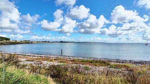 A Beautiful and Serene Coastal Landscape Featuring a Cloudy Sky and a Fisherman at Work
