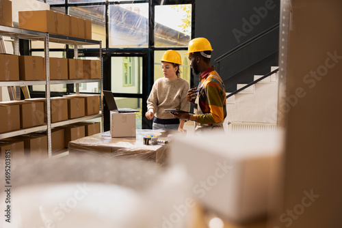 Fotografie E-shop owner and employee in coveralls preparing cardboard boxes for shipment, ensuring quality control of merchandise for online shopping distribution and custom order delivery