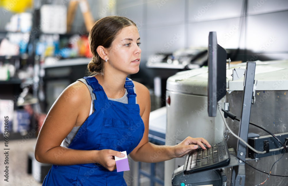 Fototapeta premium Experienced young woman seller using technical computer and mixing machine in hardware store