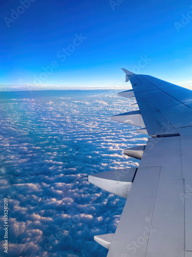 Passenger view of an airplane wing illuminated by sunrise above a dense blanket of clouds during high-altitude flight