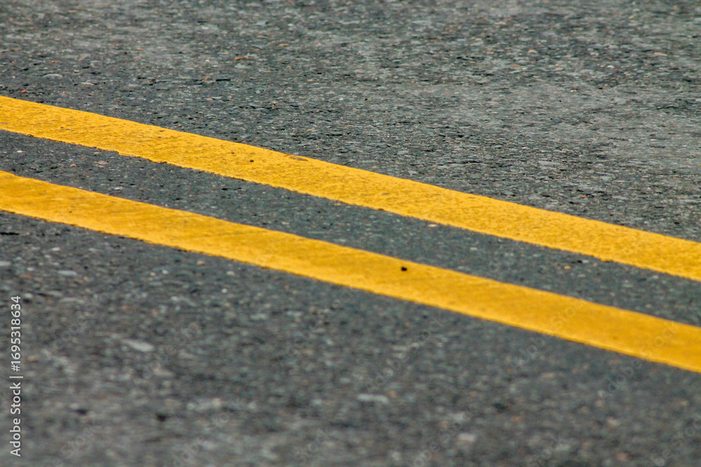 Fototapeta premium Yellow Lines on a Winding Road. Abstract turning road background with tires track and yellow striped road marking on dark asphalt. 