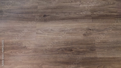 A close-up image of a wooden floor with a natural grain pattern. The smooth surface features a warm, earthy brown tone, showcasing the beauty and texture of the wood.