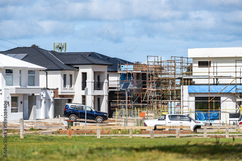 Obraz premium New residential houses under construction in suburban Melbourne, Australia, with modern homes, scaffolding on site. Concept of housing growth, urban expansion, and real estate development.