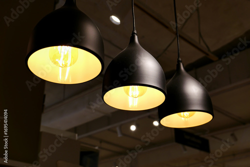 a trio of modern pendant lamps with matte black shades, hanging from a high ceiling. The bulbs emit a warm, golden glow, creating a cozy and inviting atmosphere.