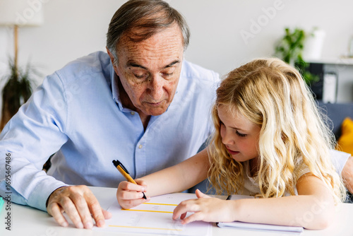 Wallpaper Mural Young little cute girl doing homework with her grandfather at home. Old man helping her daughter with school tasks. Education and family concept. Torontodigital.ca