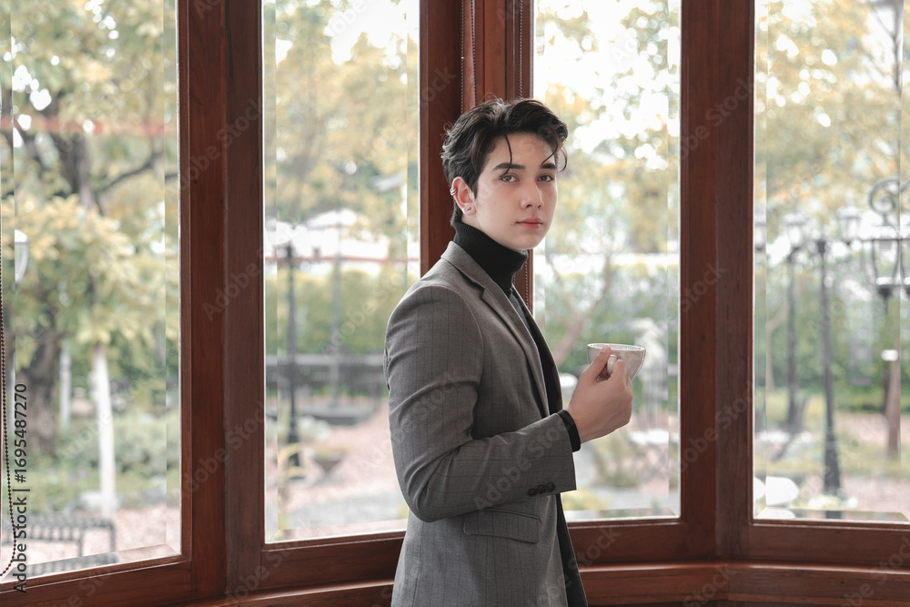 Fototapeta premium Elegant young man holding a cup in a modern indoor setting
