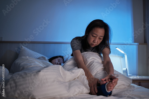 Bilde på lerret Asian single mum is sleepless, restless leg syndrome, is stressed, worried, awake at night near her child, with insomnia illness, mature and menopausal woman, family healthcare lifestyle problem