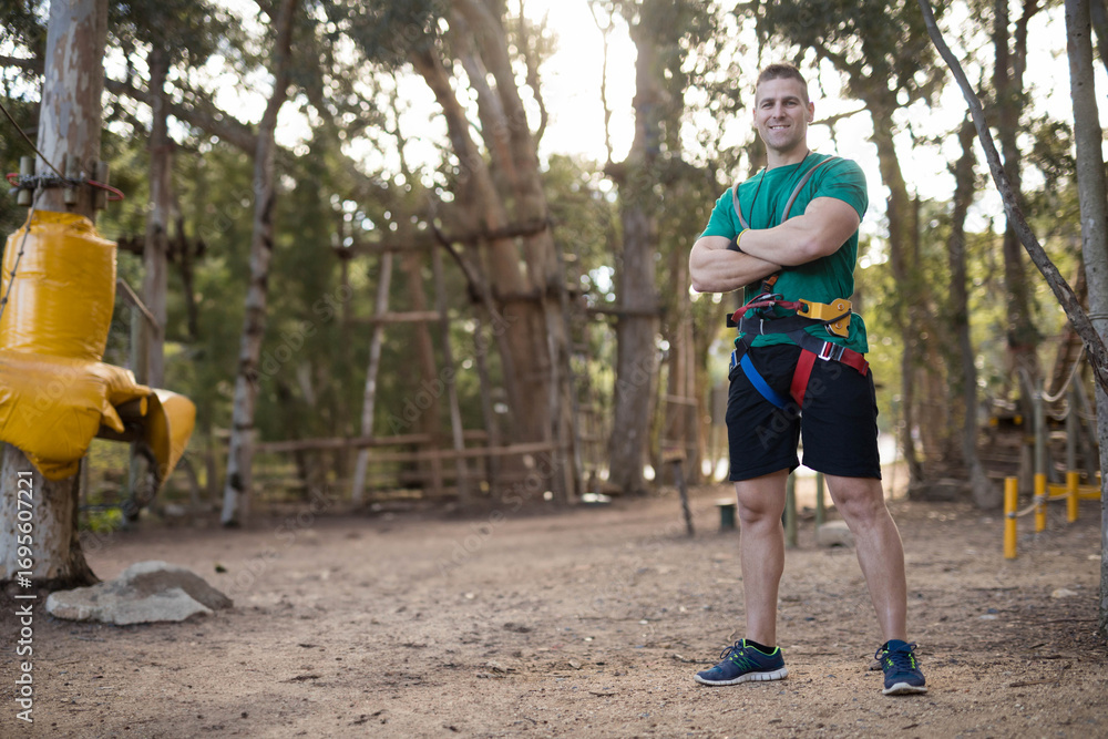Obraz premium Standing man wearing harness and carabiners at forest adventure park with rope ladders, copy space