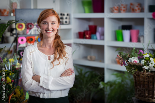 Florist standing inside floral shop, showcasing white shelves with colorful pots and ribbon spools