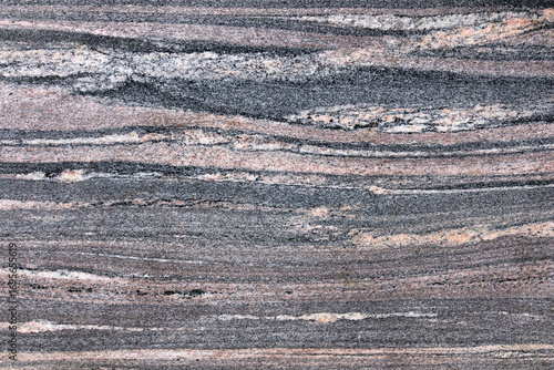 Warm hued pinkish granite with a soft flowing wavy pattern consisting of bands of pink grey and black with the rosy coloring due to the presence of alkali feldspar in the rock