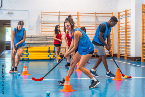 Fotografi Athletes playing floorball in a gym, dribbling with cones
