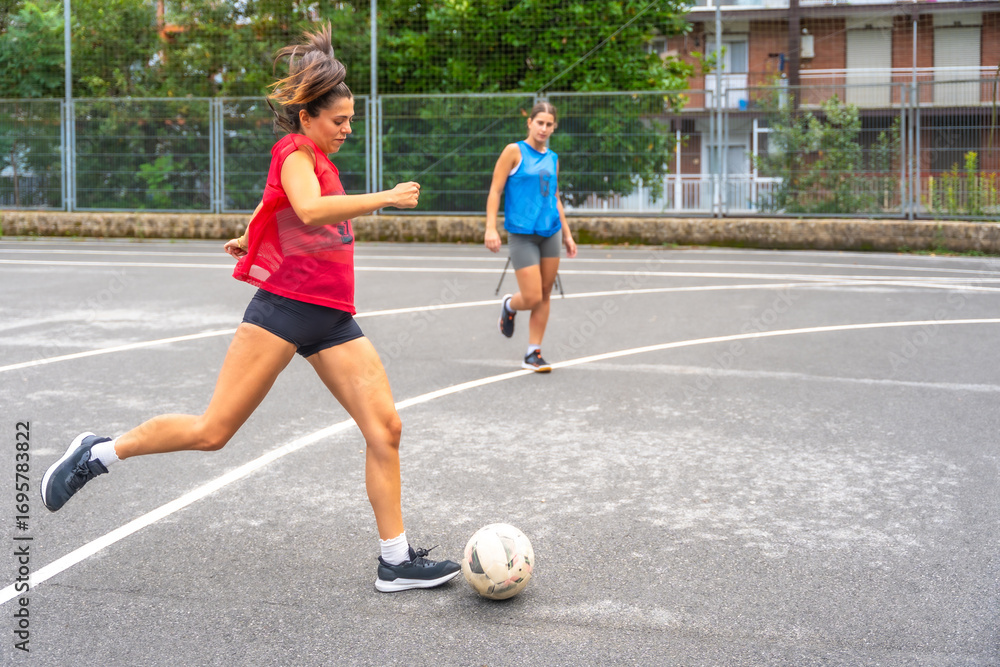 Fototapeta premium Female soccer players kicking ball on urban field