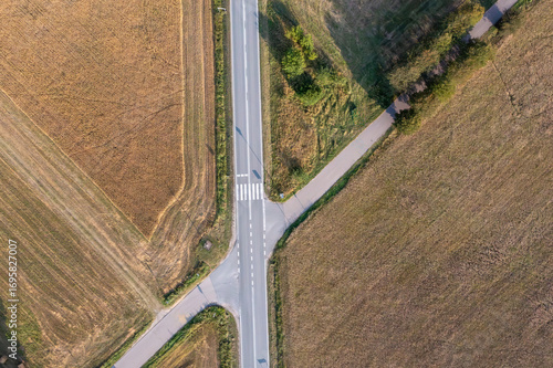 Zdjęcie lotnicze skrzyżowania dróg w otoczeniu pól uprawnych. Linie geometryczne, kontrast asfaltu i złotych pól tworzą minimalistyczny, nowoczesny krajobraz idealny do projektów o transporcie
