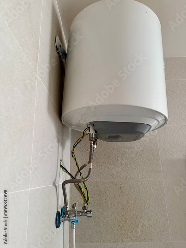 Wall-mounted electric water heater with exposed metal pipes and safety wires, modern bathroom appliance installation, plumbing, maintenance, and home repair concept