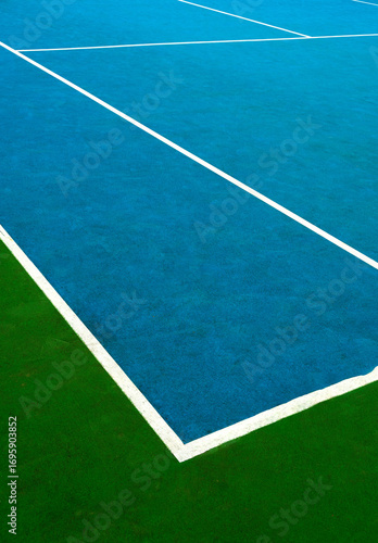 Bright colored tennis court at midday with textured surface and crisp white lines