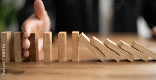 A hand halts a falling row of wooden dominoes