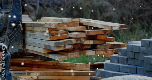 Forklift forks supporting pile of planks near stacked blocks in supply yard, snowflakes falling