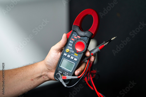 Tableau sur toile A hand holds a clamp meter with probes, showcasing electrical testing equipment