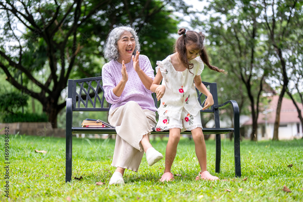 Fototapeta premium Old woman granny clapping cheering for a kid girl granddaughter dancing on grass in the park.
