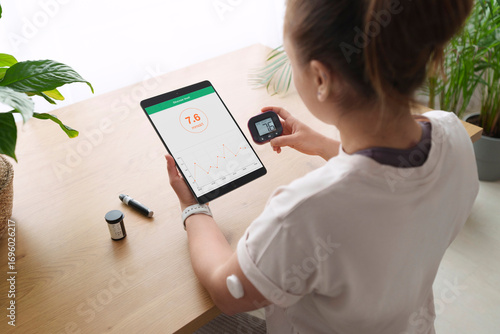 Woman with diabetes synchronizing tablet computer and glucometer at home