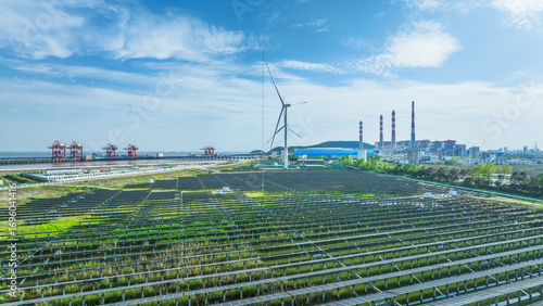 Renewable energy landscape with a solar panel farm and wind turbine coexisting with a traditional power plant.