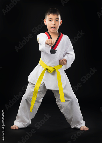 A young Asian man wearing a white taekwondo uniform with a yellow belt stands with one fist in taekwondo,